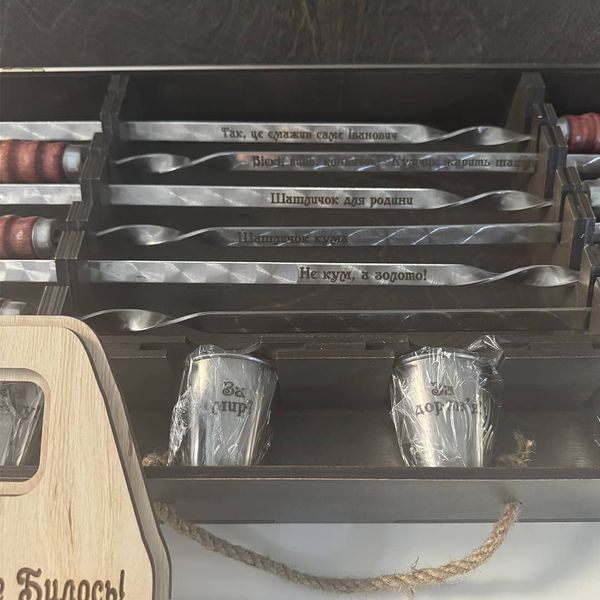 A barbecue set of skewers and shot glasses in a wooden case